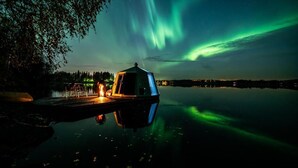 Mökki rauhallisen järven rannalla, josta avautuu näkymä revontuliin.