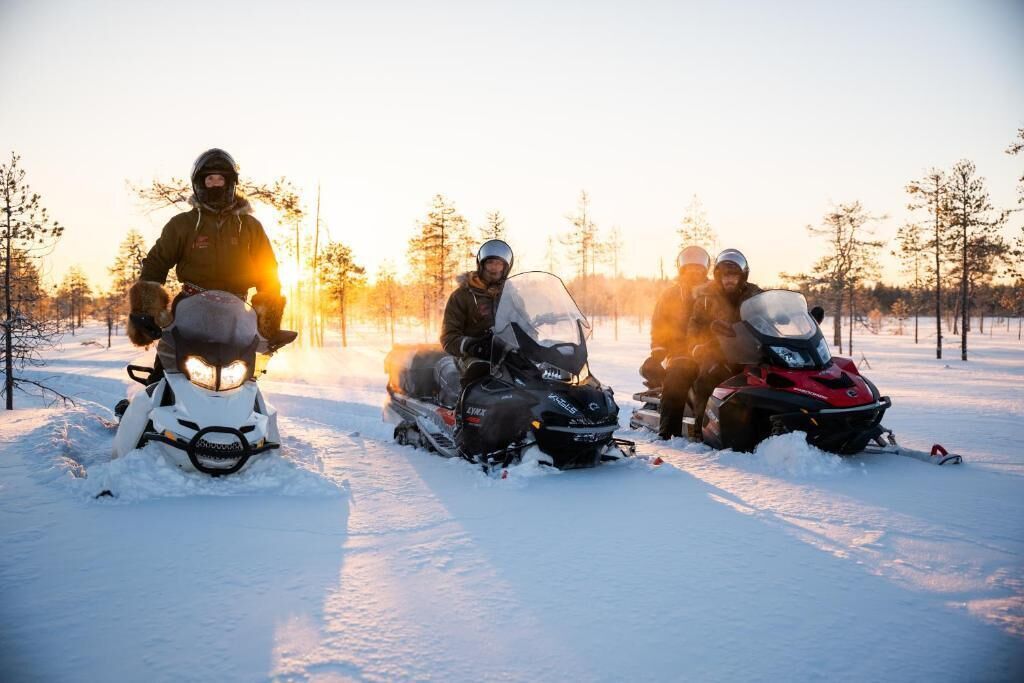 Three snowmobiles on a snowy path with trees in the background.