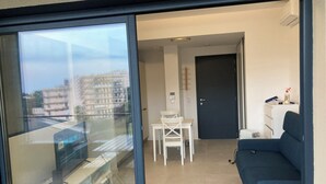 A modern apartment with a balcony, a small dining area, a dark-colored sofa, and a view of the cityscape. - Superb studio with sea view of downtown Bastia  (Bastia)