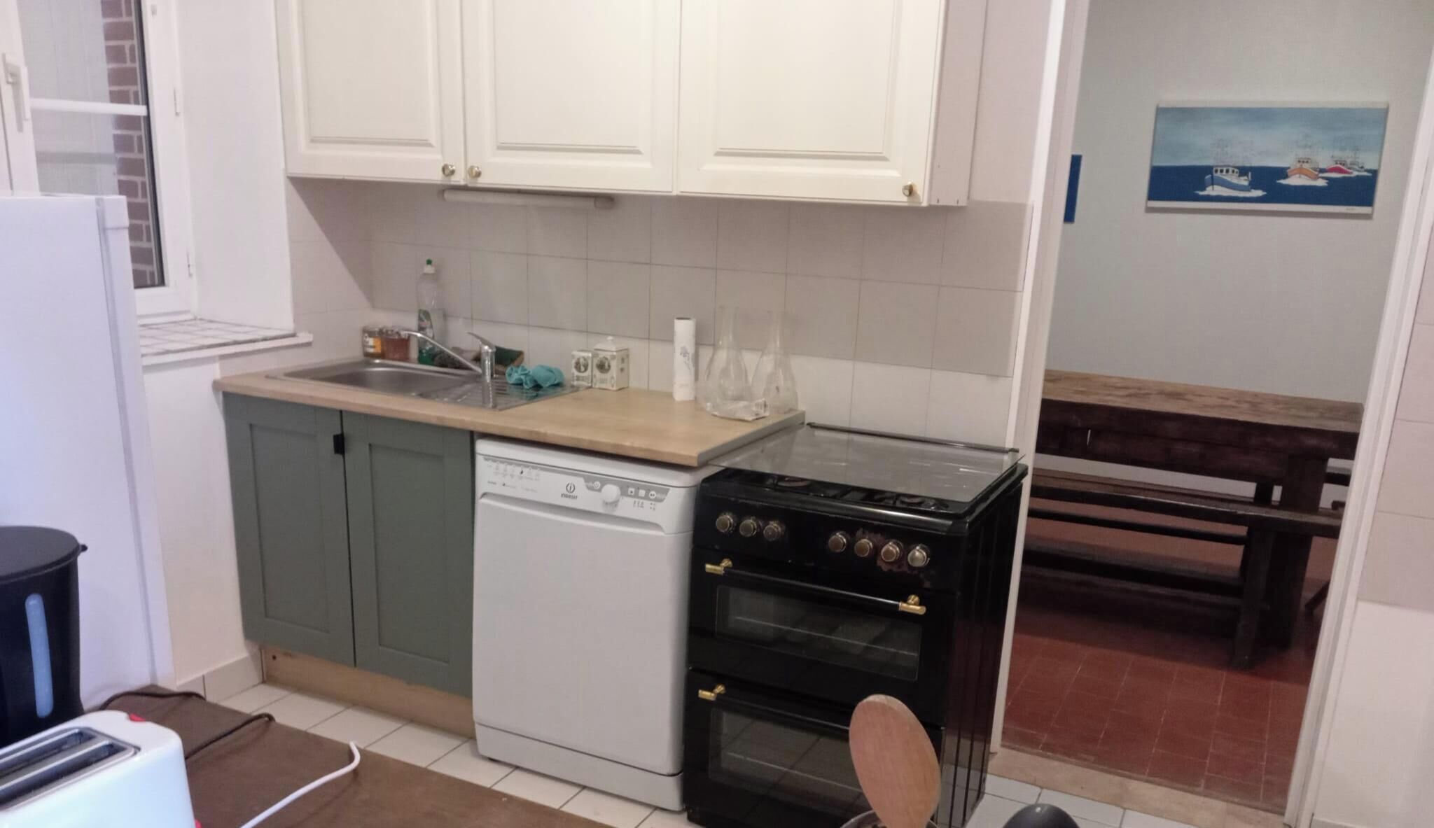Une cuisine compacte avec des meubles blancs, un lave-vaisselle, une cuisinière et un banc dans le coin repas.