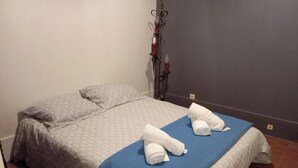 Una cama individual con una colcha azul y dos almohadas, una toalla sobre la cama, y un radiador fijado a la pared.