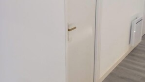 Una puerta blanca con manija dorada, el número '3' pequeño en la pared, y una pared blanca con una viga de madera arriba.