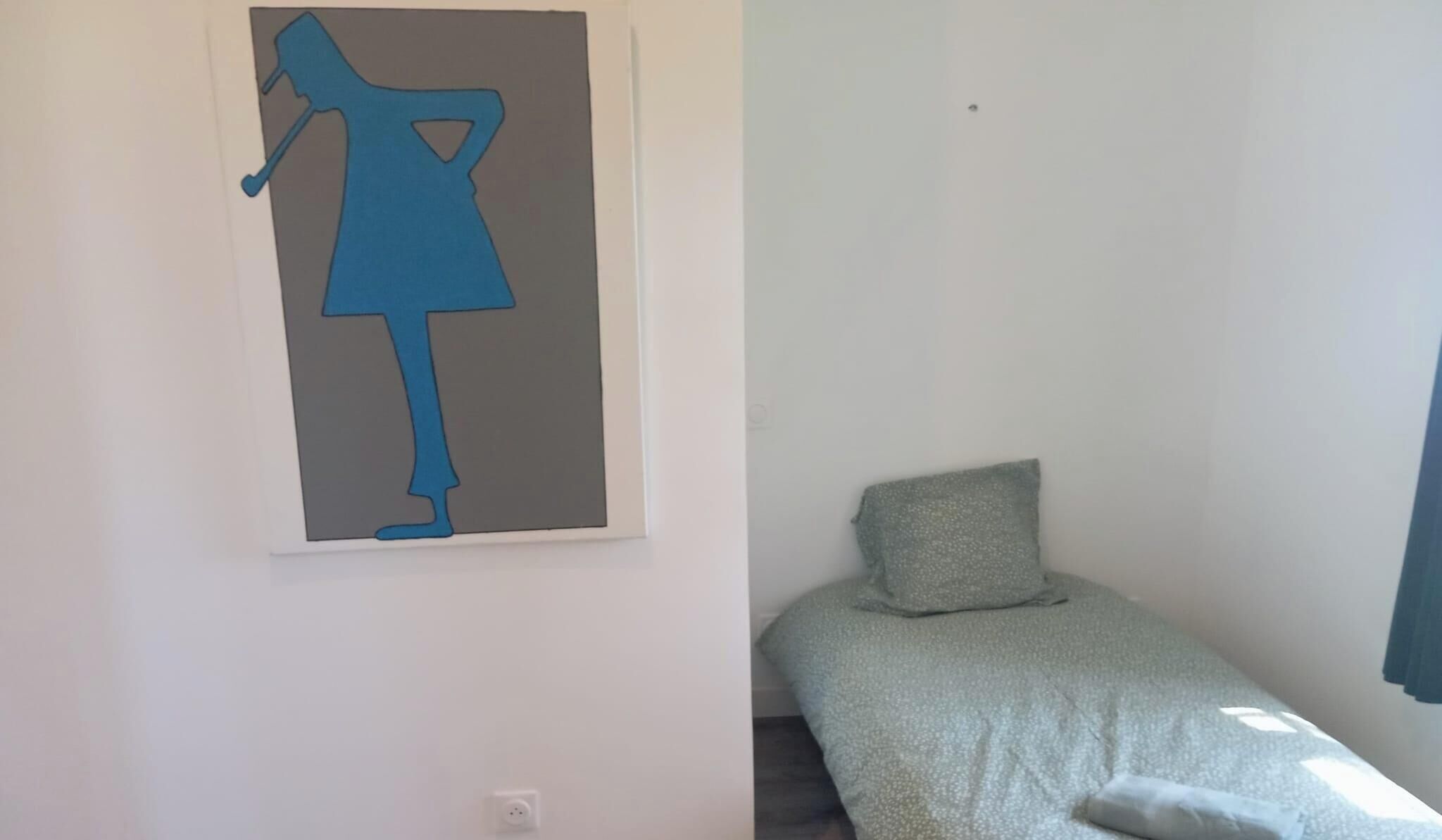 Huone, jossa on sänky, tyyny ja seinälle ripustettu taideteos.