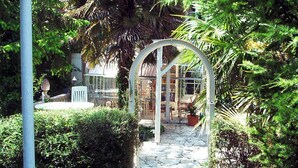 Un jardin avec un sentier de pierres menant à une structure en verre, le tout entouré d’une végétation luxuriante.