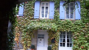 Un bâtiment avec des volets bleus, une porte blanche et une fenêtre ornée d’une grille métallique.