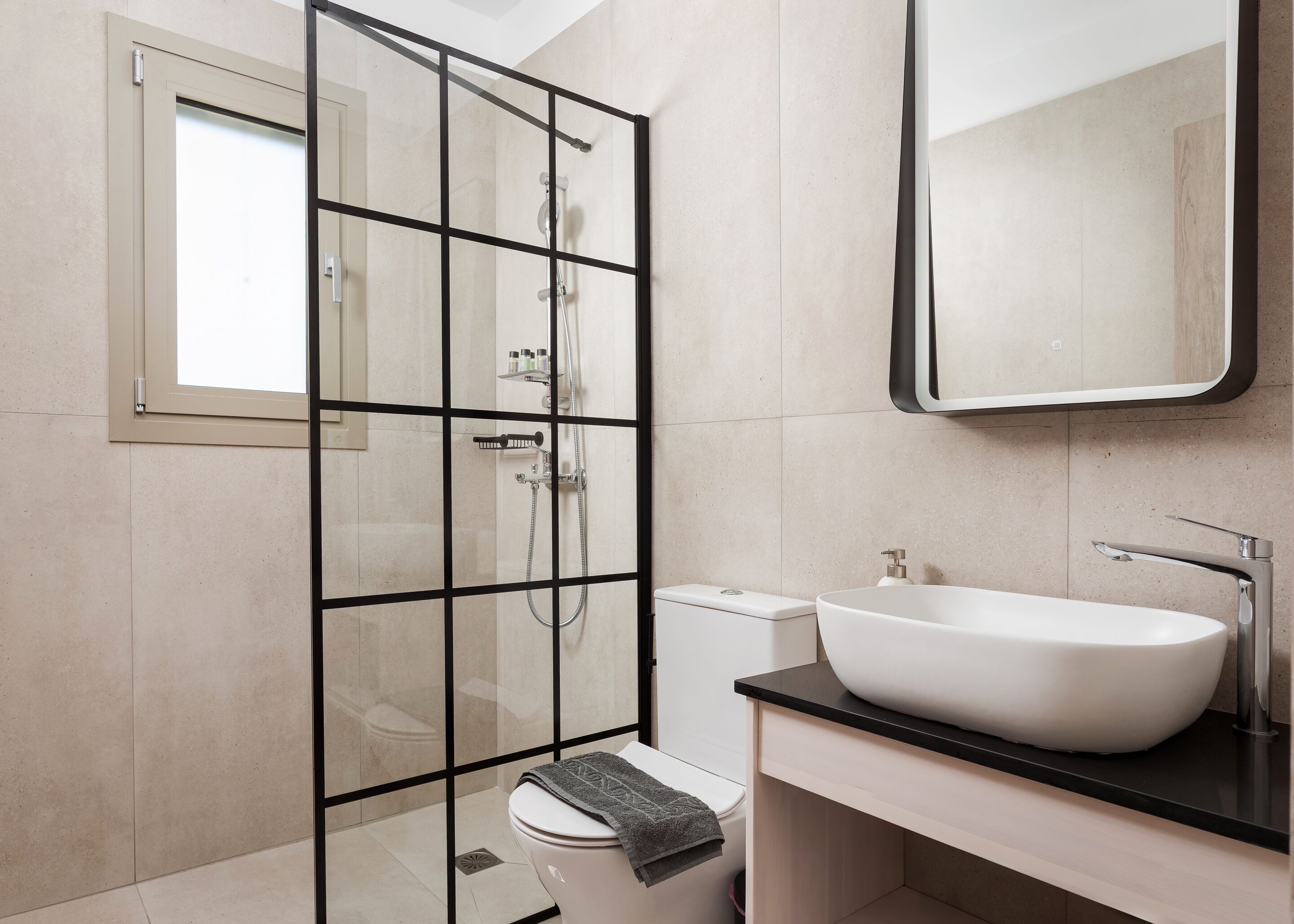 Een moderne badkamer met een glazen douchecabine, een wit toilet, een wastafel met een ruime wasbak en een spiegel boven de wastafel.