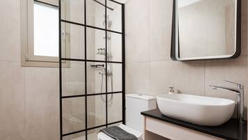 Een moderne badkamer met een glazen douchecabine, een wit toilet, een wastafel met een ruime wasbak en een spiegel boven de wastafel.