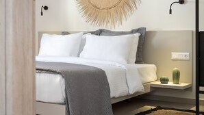 Un dormitorio moderno con cama, una lámpara de pared, un tapiz texturizado y un pequeño cactus en una mesita de noche.