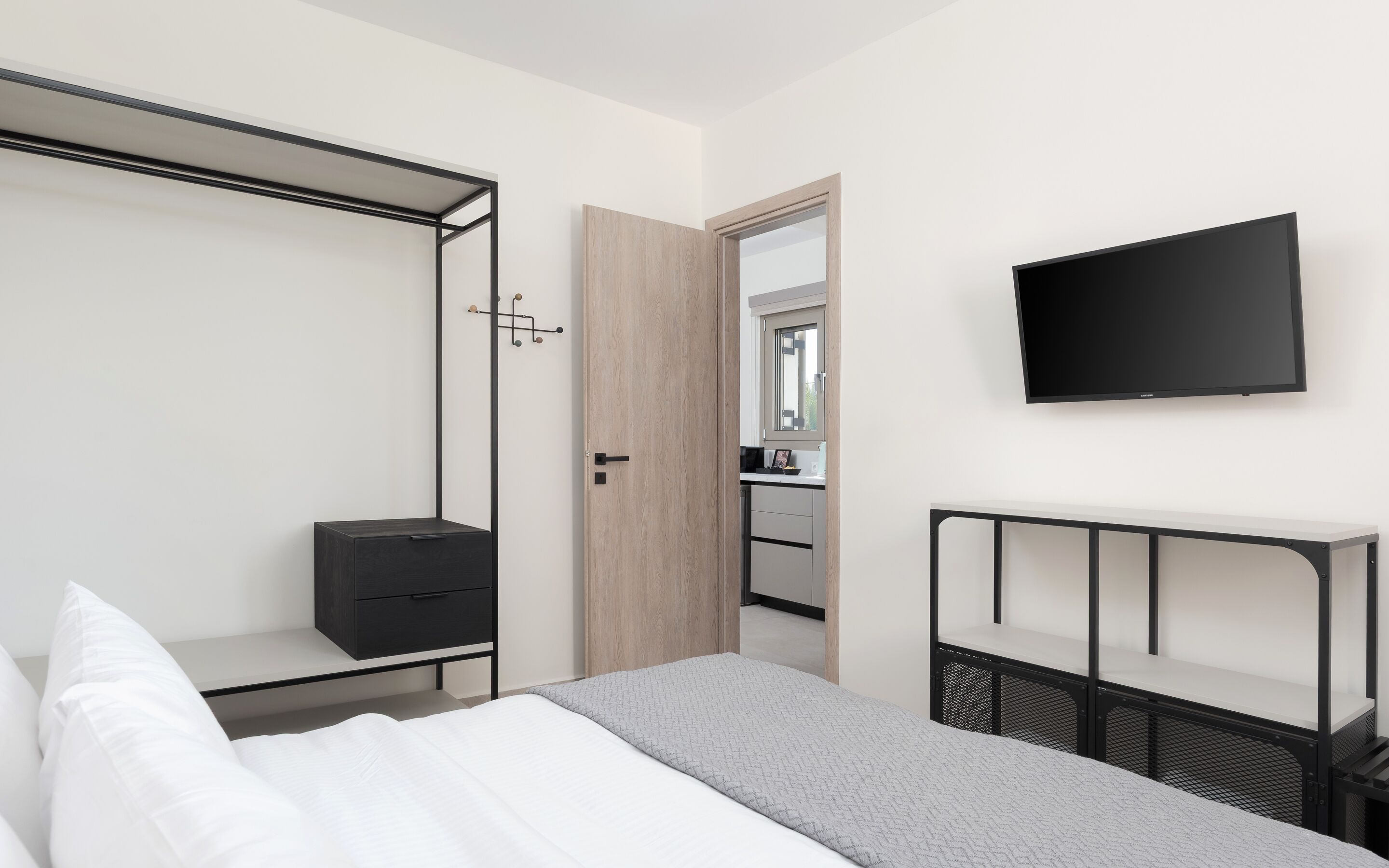 A modern hotel room with a bed, a TV, a wardrobe, and a bathroom visible through an open door.