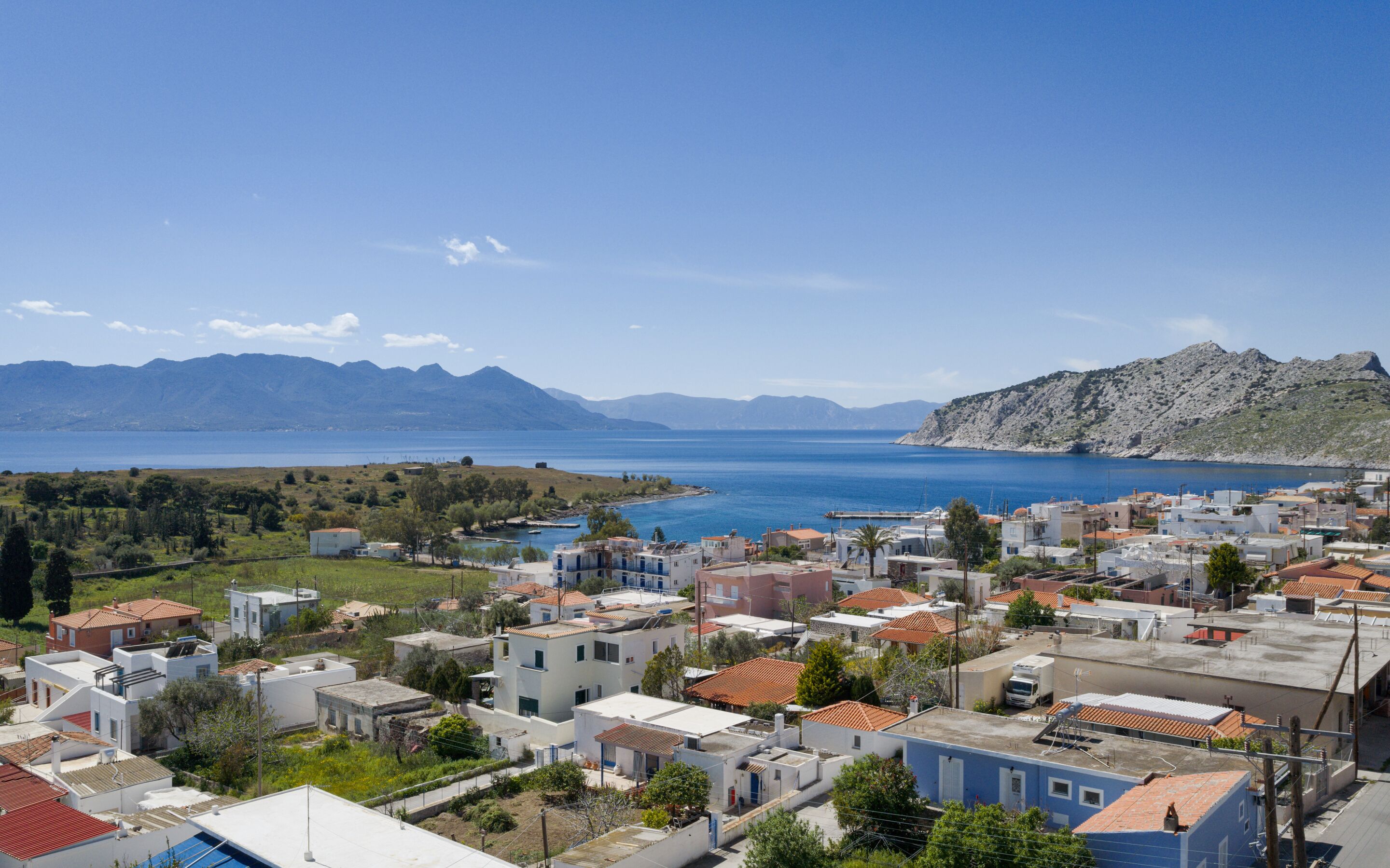 Un pueblo costero con edificios, un mar azul cristalino y montañas al fondo.