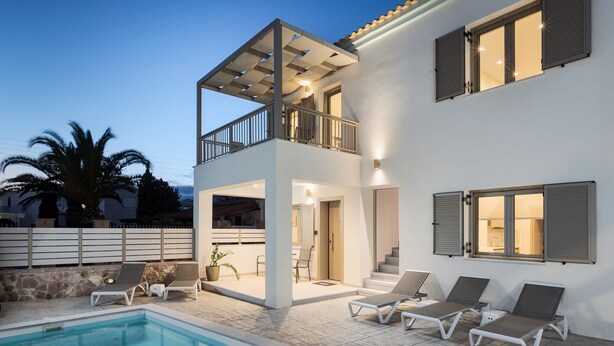 Una casa de dos pisos con piscina, mobiliario exterior y un balcón.