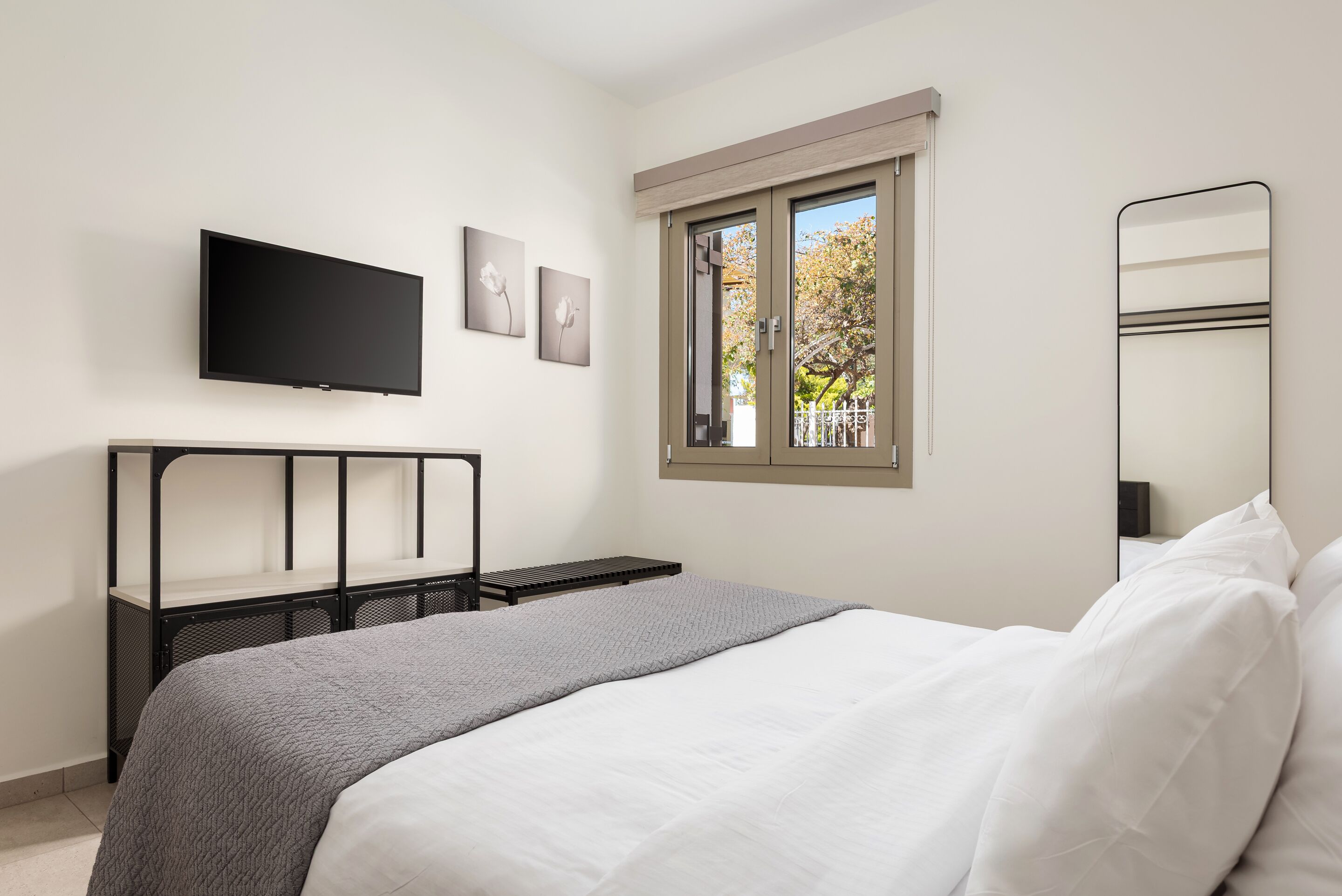 Una camera da letto con un letto, una TV a parete, una finestra e uno specchio.