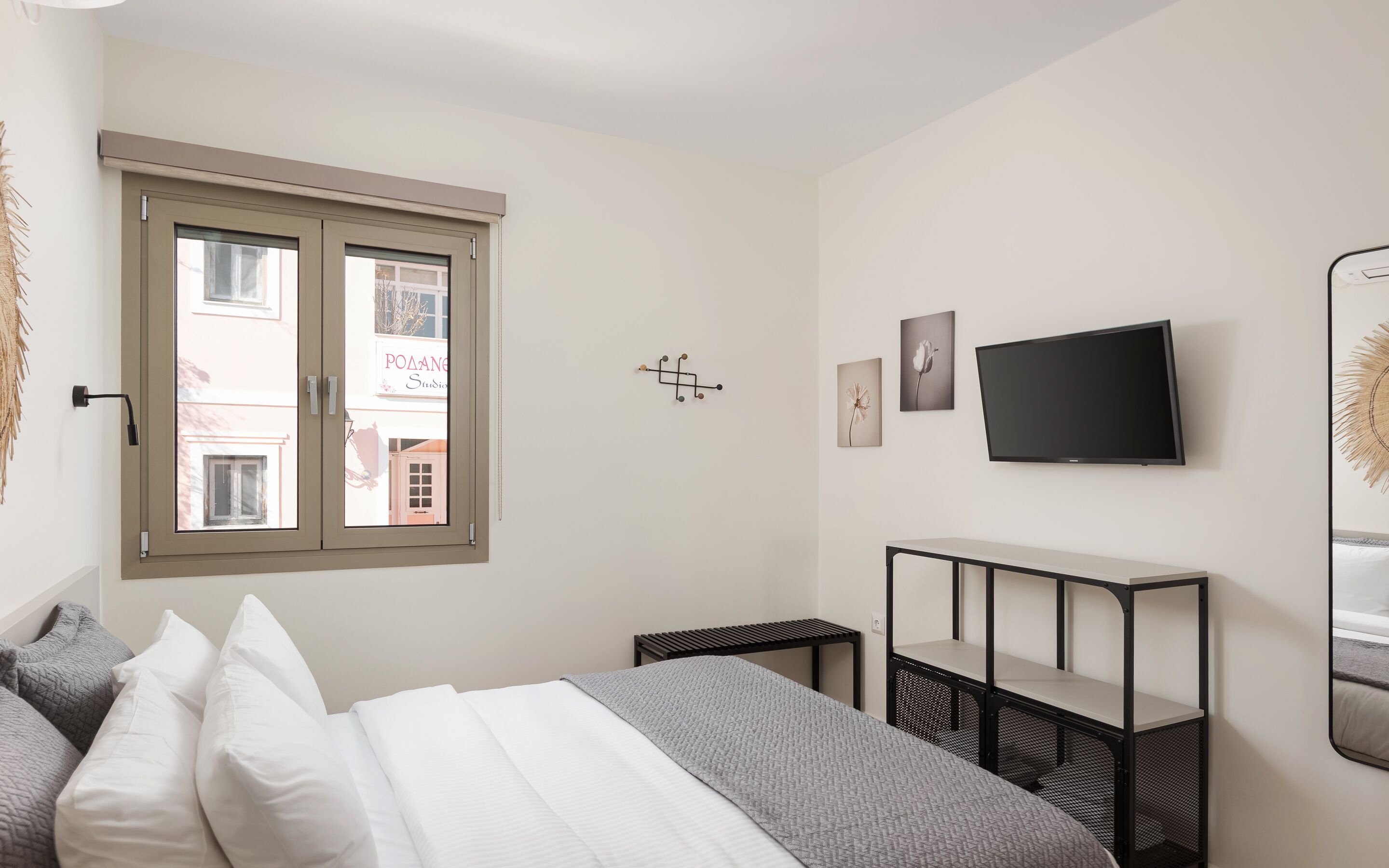 A bedroom with a bed, a TV, a window, and a wall-mounted shelf.