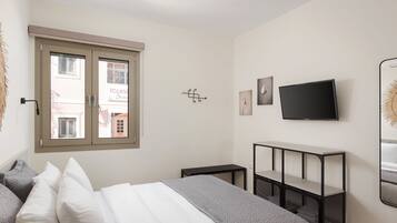 A bedroom with a bed, a TV, a window, and a wall-mounted shelf.