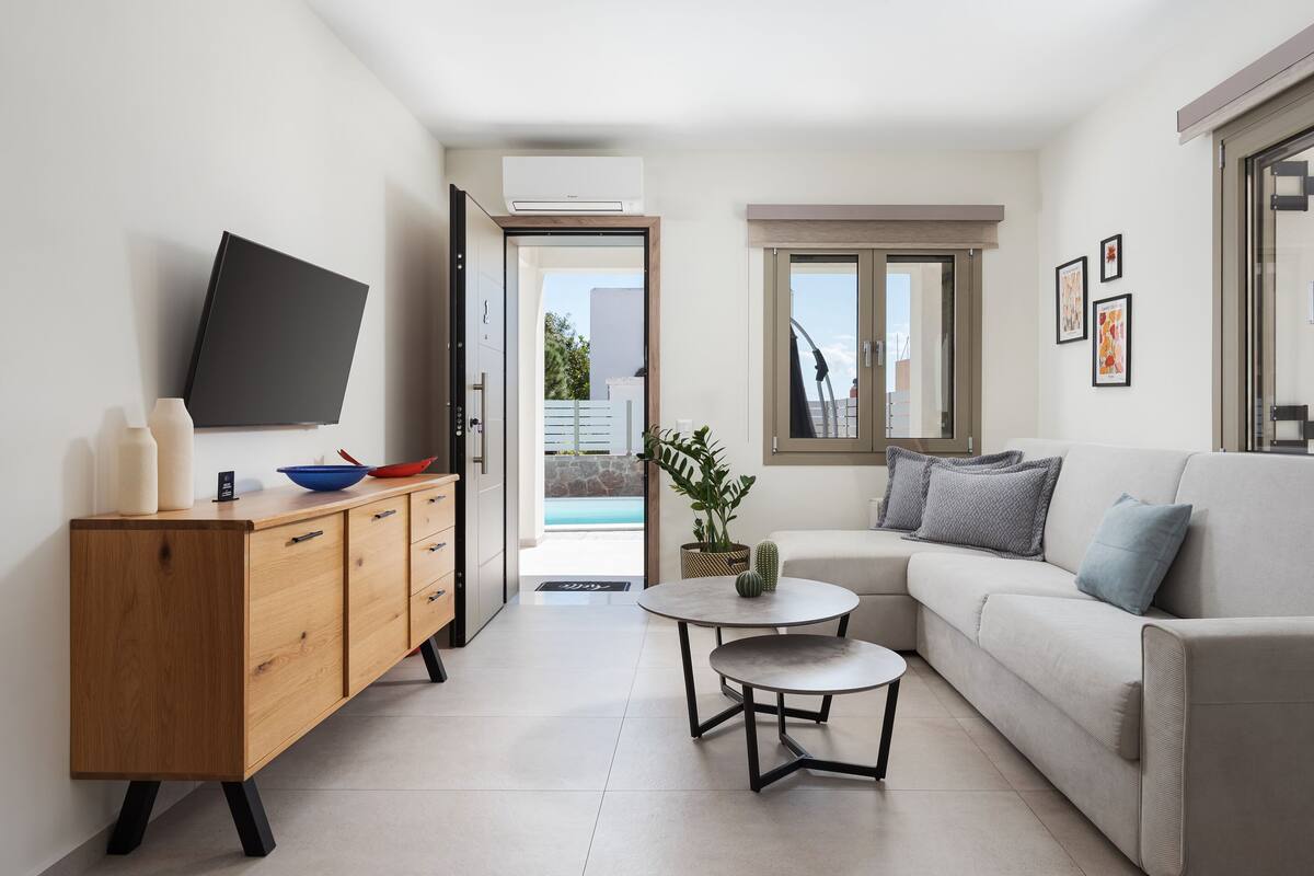 Un salon moderne avec un canapé, une table basse, un téléviseur fixé au mur et un meuble en bois.