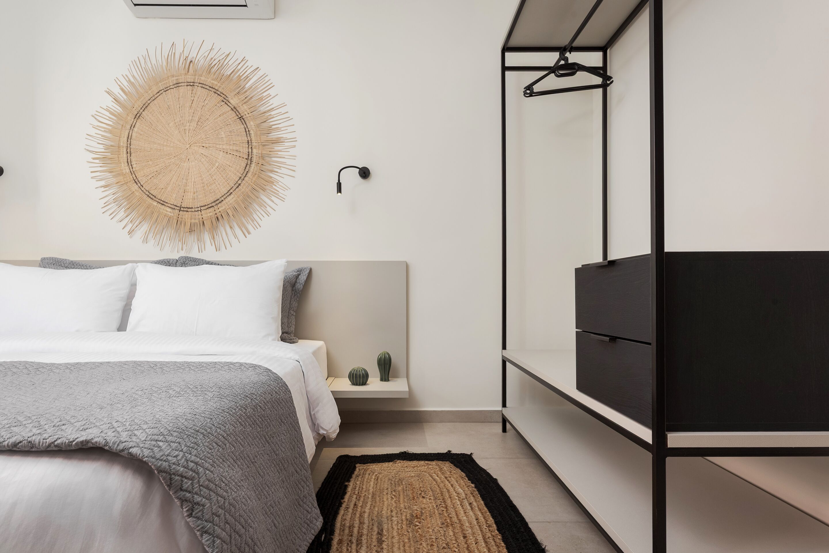 A bedroom with a bed, bedside tables, a wall-mounted light, a mirror, and a black wardrobe.