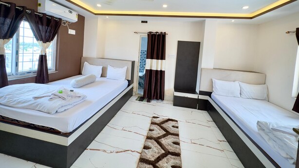 A hotel room with two beds, an air conditioning unit, a ceiling fan, a bathroom with a shower curtain, and a patterned rug. - Hotel BN Palace  (Barakpur)