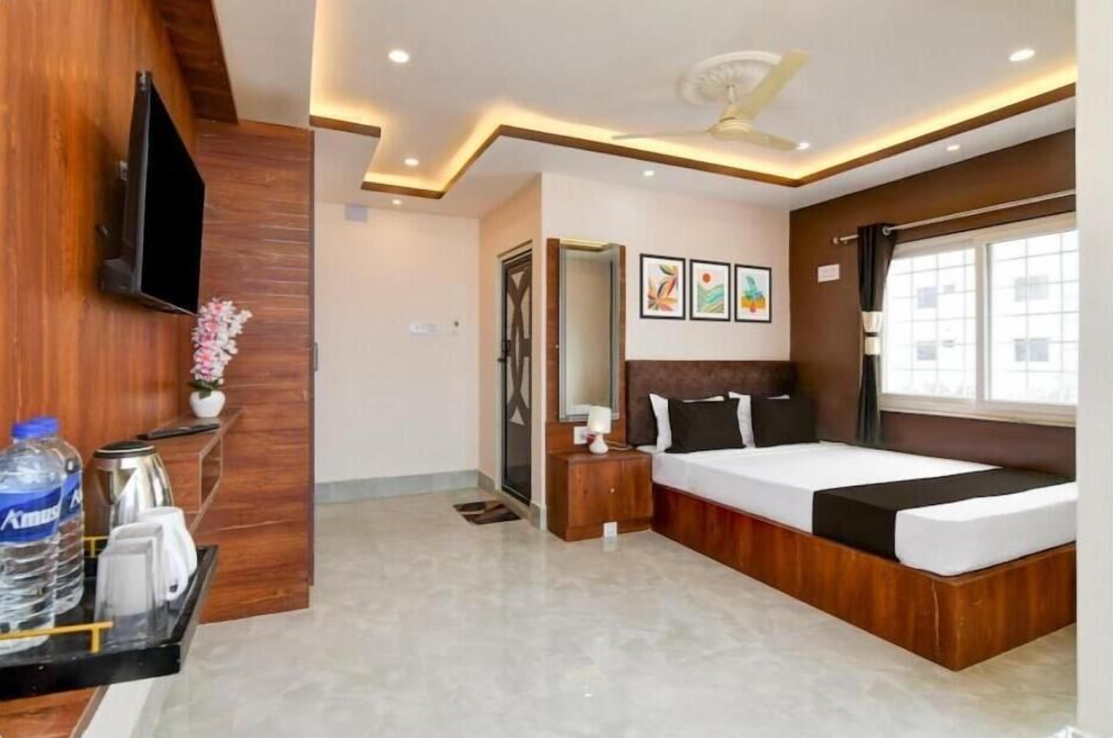 A modern hotel room with a bed, bedside table, TV, artwork, and a window.