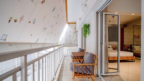 Een balkon met een witte reling, een rieten stoel, een tafel en een bloempot met plant.