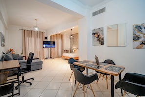 Ein modernes Wohnzimmer mit Fernseher, einer Couch, einem Esstisch, Stühlen und Kunstwerken an den Wänden.