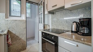 Een keuken met granieten werkbladen, een ingebouwde oven, een koffiezetapparaat en een raam met zonwering.