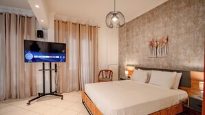 Een slaapkamer met een bed, een televisie op een dressoir, gordijnen, een wandlamp en een schilderij.