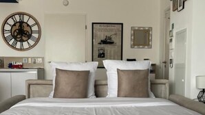 Ein Hotelzimmer mit einem großen Bett, einer Wanduhr, einem gerahmten Bild und einem Spiegel.