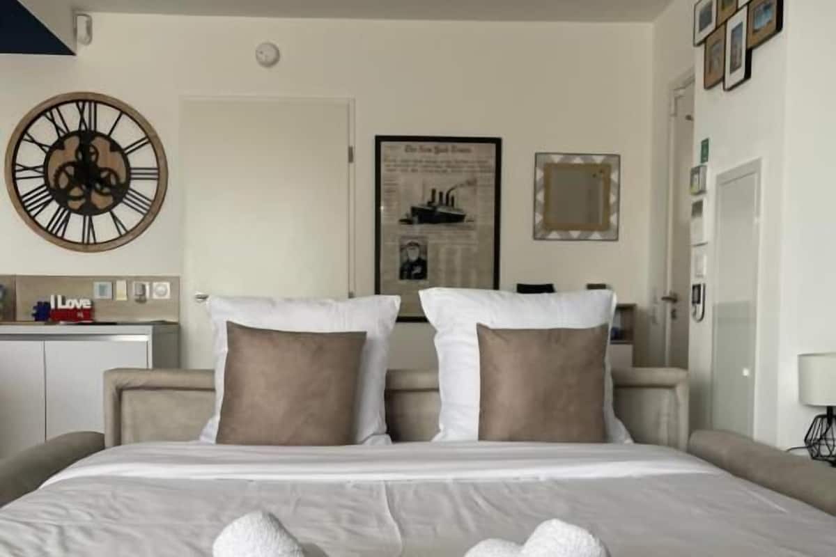 A hotel room with a large bed, a wall clock, a framed picture, and a mirror.
