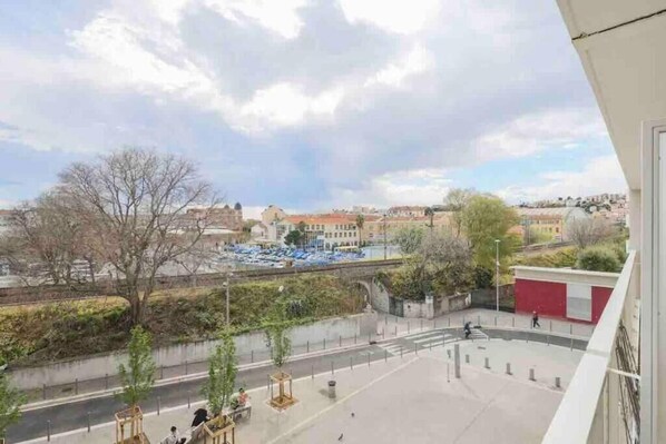 A view from a balcony overlooking a cityscape with buildings, a river, and a park area.