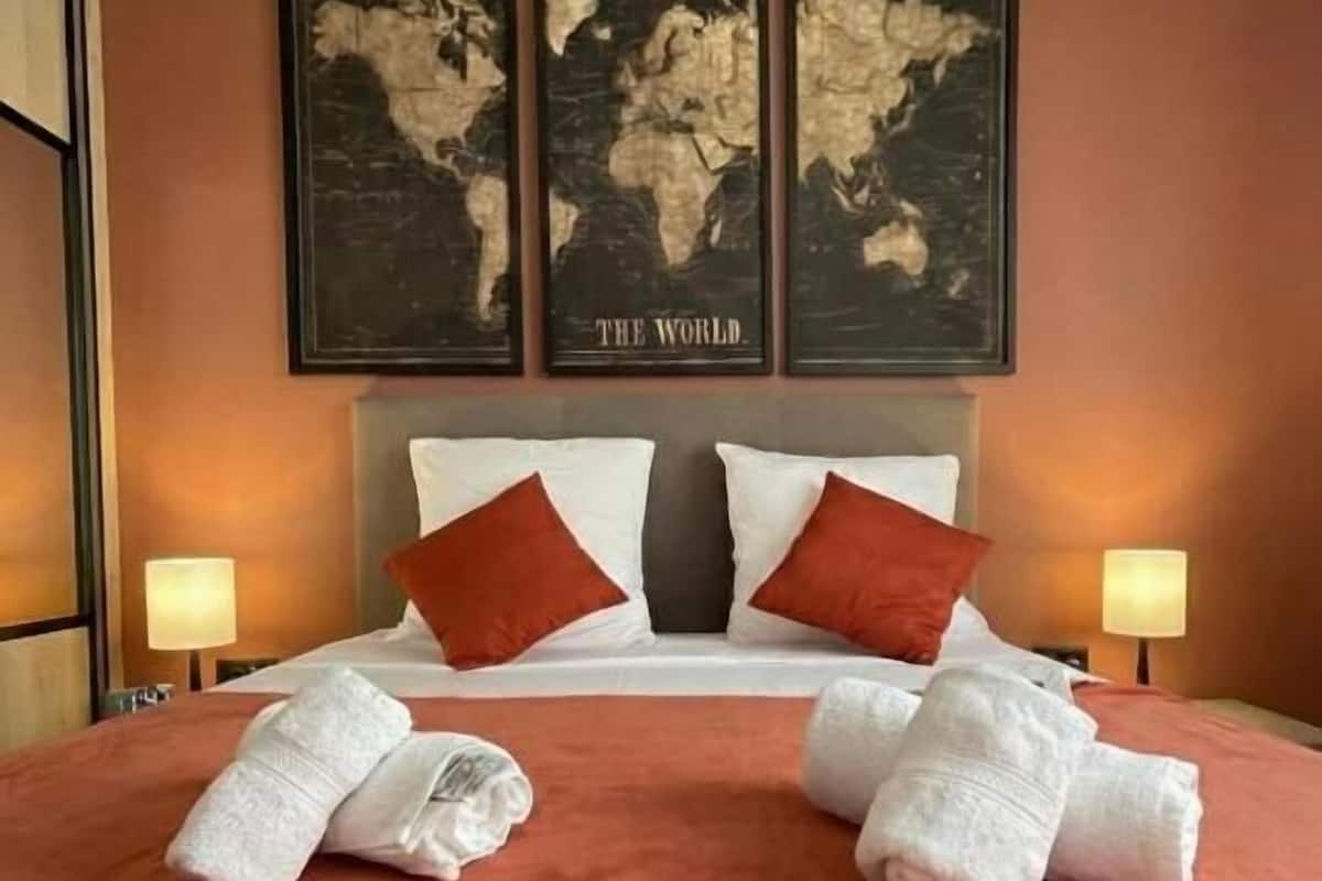 A hotel room with a large bed, two pillows, a world map on the wall, and two lamps on either side of the bed.