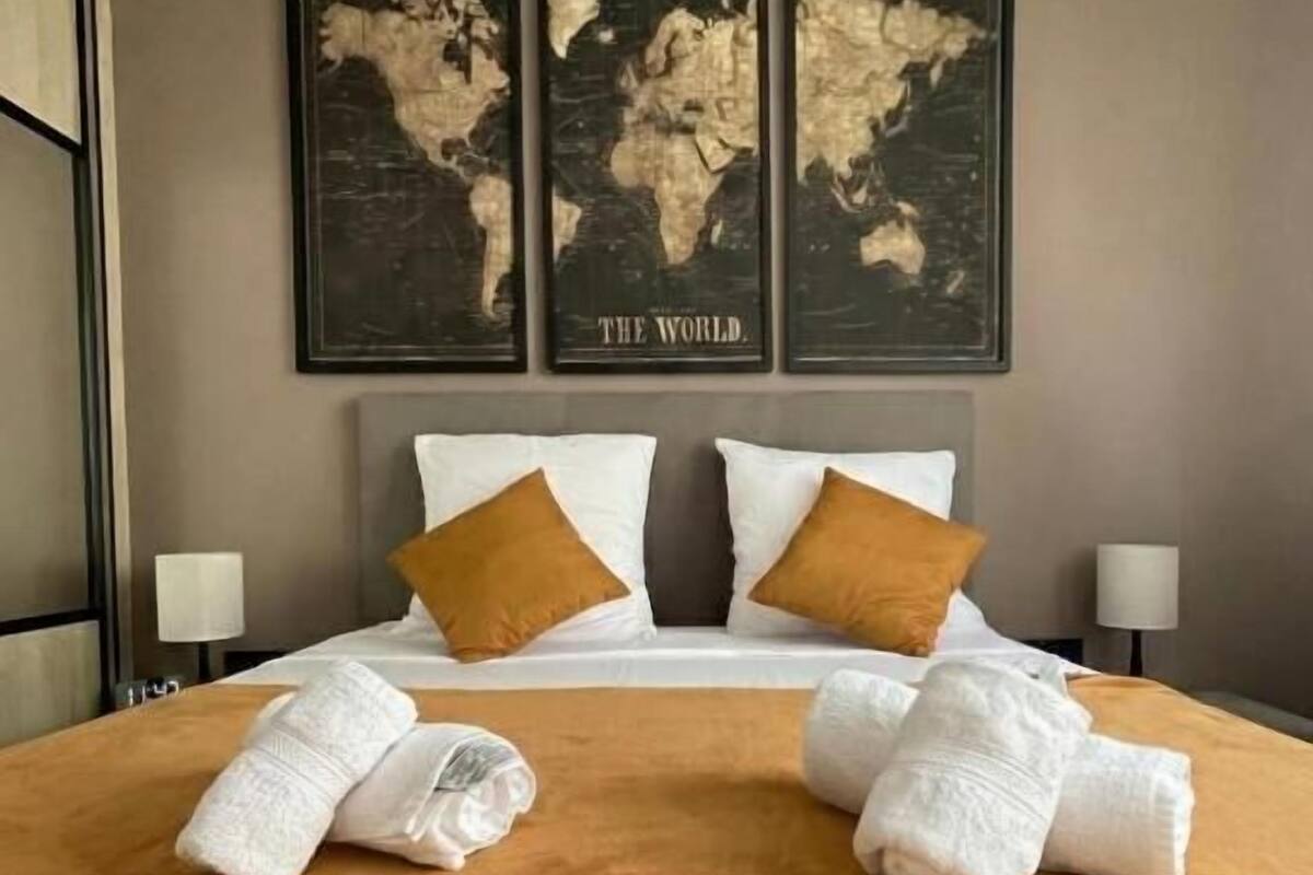 A hotel room with a large bed, two pillows, a world map on the wall, and two lamps.