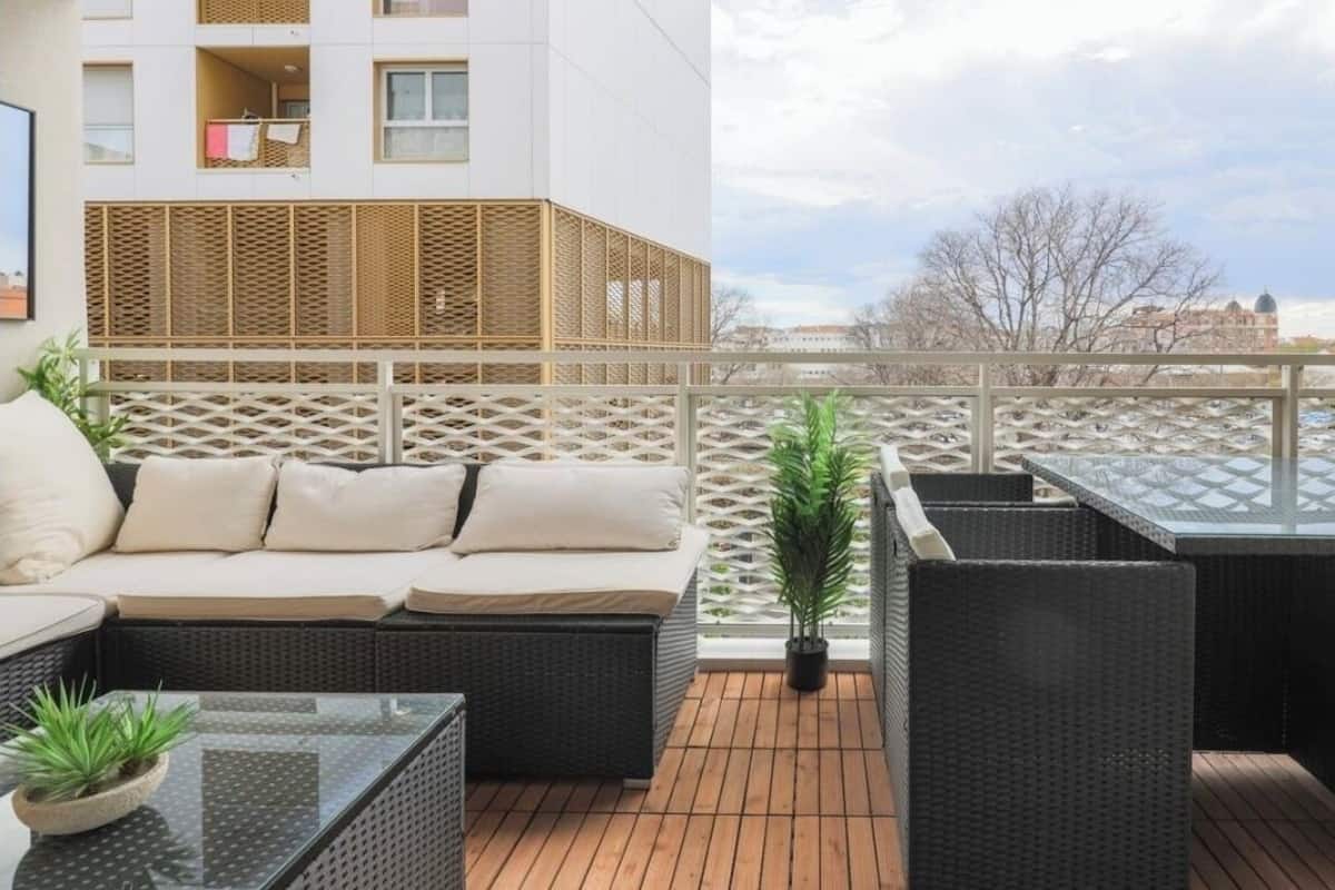 A rooftop terrace with wicker furniture, a potted plant, and a view of buildings.