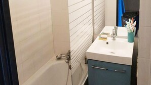 A bathroom with a bathtub, a sink with a cup of toothbrushes, and a blue cabinet. - 2 Rooms for 6 People (Huez)
