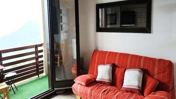 A room with a red sofa, a small table, a chair, a sliding glass door leading to a balcony, and a framed picture on the wall. - 2 Rooms for 6 People (Huez)