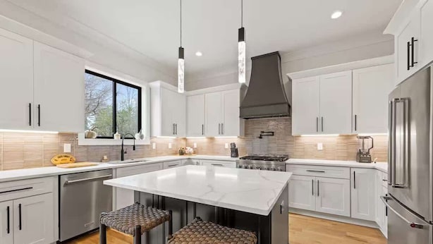 A modern kitchen with white cabinets, a large island, stainless steel appliances, and woven bar stools. - New Build | Chef's Kitchen | Fireplace | 4BR (Charlotte)