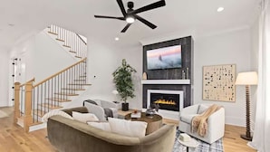A modern living room with a sofa, coffee table, fireplace, TV, and a staircase. - New Build | Chef's Kitchen | Fireplace | 4BR (Charlotte)