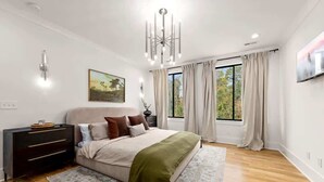 A bedroom with a bed, bedside table, lamp, curtains, and a painting on the wall. - New Build | Chef's Kitchen | Fireplace | 4BR (Charlotte)