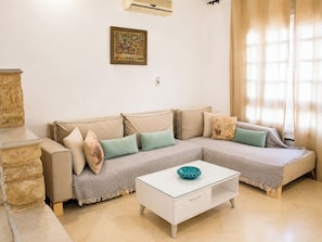 A living room with a sectional sofa, a white coffee table, and a stone accent piece. - Charming 600m2 villa with large garden and swimming pool (La Soukra)
