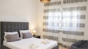 Een net opgemaakt bed met kussens, een bedlampje en een raam met gestreepte gordijnen.
