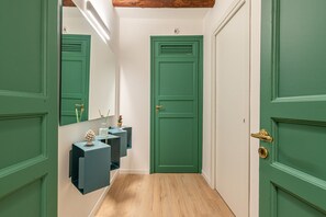 Een gang met groene deuren, een spiegel en een klein blauw plankje met decoratieve objecten.
