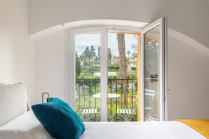 Une chambre à coucher avec un lit, un oreiller turquoise, un matelas blanc et un balcon avec une table et des chaises.