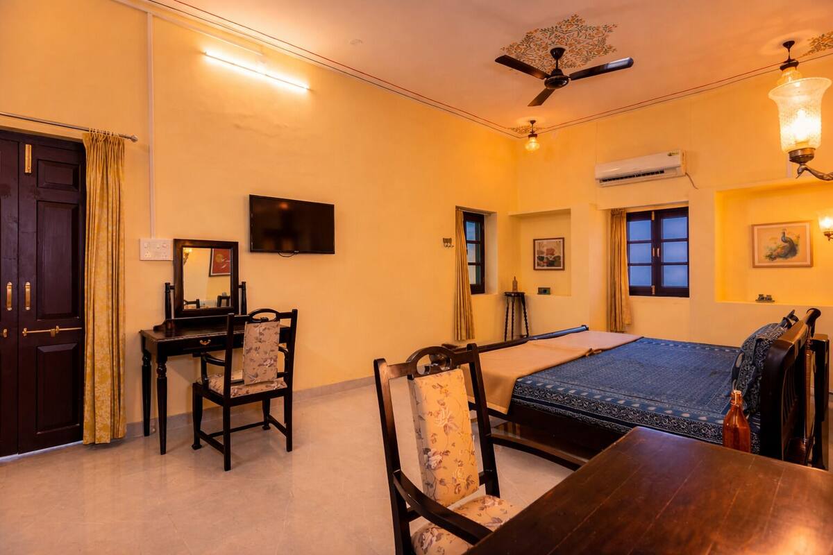 Ein Hotelzimmer mit Bett, Schreibtisch, Stuhl, Deckenventilator, Klimaanlage und Fenster.