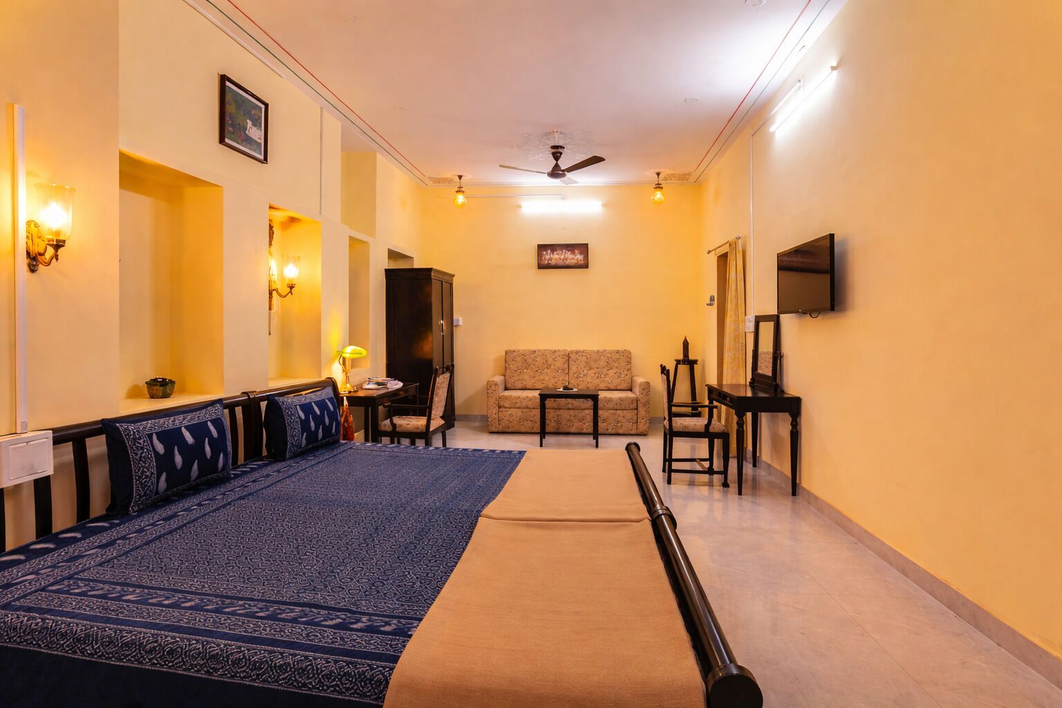 Habitación de hotel con cama, sofá, televisión, ventilador de techo y pasillo con lámpara.