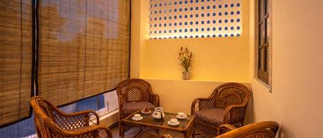A room with a table set for tea, four wicker chairs, a potted plant, and a wall with a perforated design.
