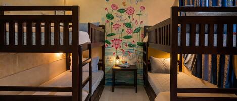 A room with bunk beds, a small table with a lamp, and a mural with birds and flowers.