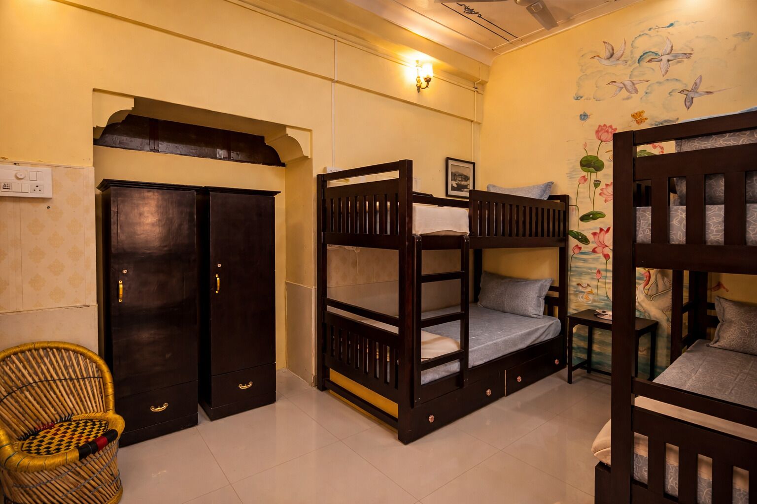 A room with bunk beds, a wicker chair, a wardrobe, and a wall with a floral mural.