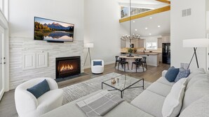 Amplia sala de estar con chimenea, televisor montado en la pared y una cocina moderna al fondo.