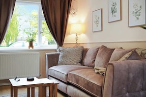 Ein Wohnzimmer mit einer Couch, einem Tisch, einer Lampe und gerahmten Pflanzenbildern an der Wand.