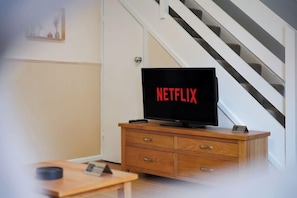 Ein Zimmer mit einem HolztV-Schrank, einem Flachbildfernseher, der 'NETFLIX' zeigt, und einer Treppe im Hintergrund.