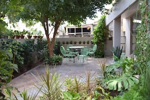 A patio with a table and chairs, surrounded by potted plants and trees.